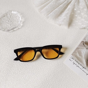 Gros plan de lunettes de soleil carrées noires avec verres jaunes sur fond blanc