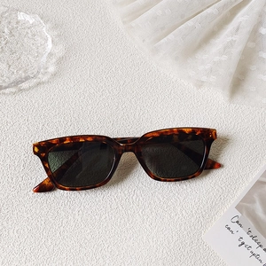 Lunettes de soleil rétro écaillées avec verres vert foncé sur fond texturé blanc
