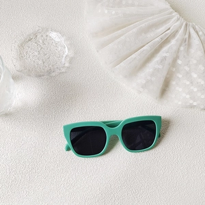 Close-up of mint green square sunglasses with dark lenses on a white lace background