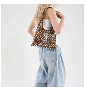 Brown leather hobo tote bag with silver metal rivets worn on shoulder by a model