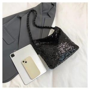 Close-up of black sequined bucket bag with braided strap on white fabric background