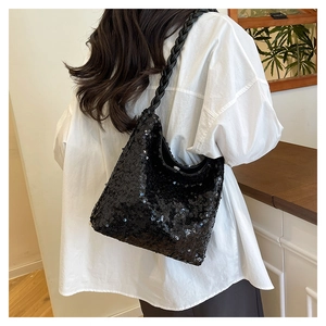 Detail of black sequined bucket bag with thick braided leather strap on a model