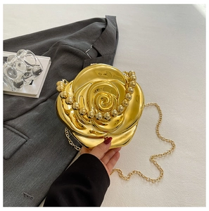 Detail of a 3D gold rose clutch bag with metallic flower petals and pearl handle strap