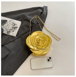 Detailed view of golden rose-shaped acrylic clutch bag with metal chain beside a smartphone