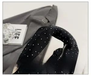 Close-up of black pleated tote bag with silver metal studs and knotted handle detail