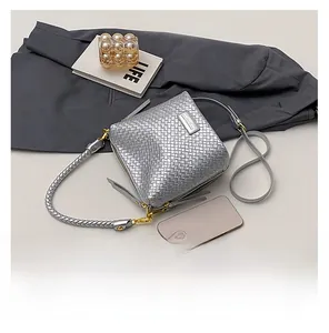 Detailed view of silver woven shoulder bag with metallic logo plate and zipper closure