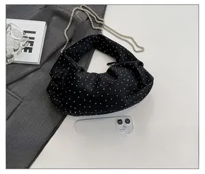 Top view of black pleated chain bag with white studs on a grey suit jacket