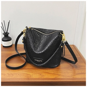Detail of black woven leather bucket bag with gold hardware and logo on wooden surface