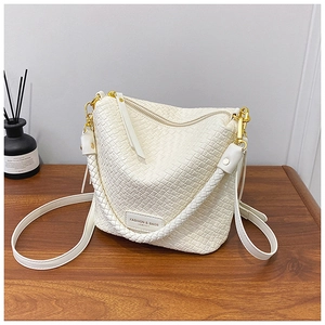 Detailed close-up of cream woven bucket bag with gold hardware on wooden surface