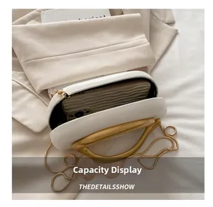 Capacidad interna del bolso caja de cuero blanco con asa dorada y un smartphone