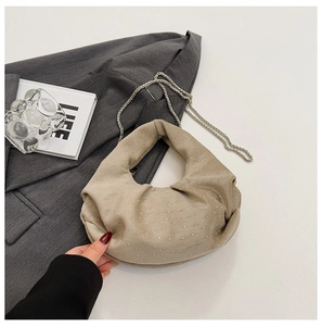 Close-up of beige pleated dumpling bag with silver studs and sleek metal chain strap