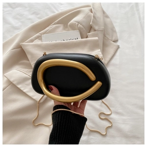 Detalle de bolso de mano en cuero negro con asa de anillo dorado grande y cadena