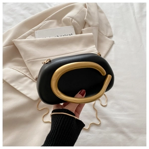 Detalle de bolso de cuero negro con asa metálica grande en forma de C dorada y cadena