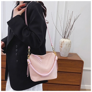 Detailed view of pink woven bucket bag featuring tassel and adjustable shoulder strap
