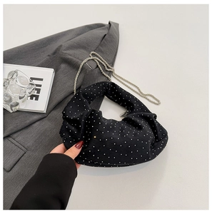 Detail of black mini handbag with silver studs on a grey suit jacket and metal chain