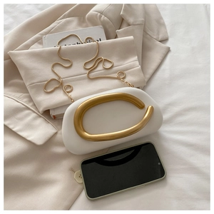Detalle de bolso de mano blanco con asa dorada curva y correa de cadena de serpiente