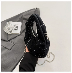 Close-up of black pleated dumpling bag with silver rivets and metal chain strap
