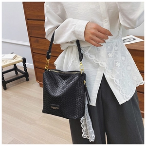 Detail of black woven bucket bag with gold hardware shown in a professional work setting