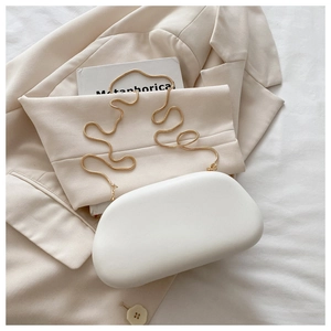 Detalle de un bolso de noche blanco tipo nube con elegante cadena de serpiente dorada sobre blazer