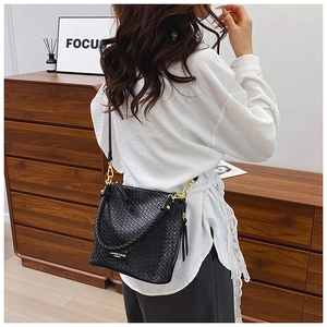 Detail of black woven leather bucket bag featuring gold hardware and a braided top handle