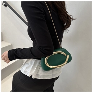 Detalle de bolso ovalado verde oscuro con asa de anillo dorada y cadena en modelo