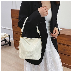 Detail of a beige woven bucket bag showing fine craftsmanship and gold-tone metal hardware