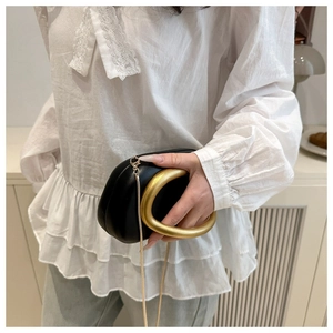 Detalle de bolso caja de cuero negro con asa de metal dorado grande y correa de cadena