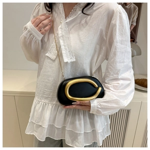 Detalle de un elegante bolso negro con cierre metálico en forma de C dorado y cadena fina