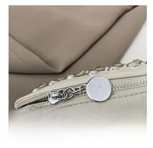 Détail de la fermeture éclair en métal et des strass sur le sac à bandoulière couleur crème