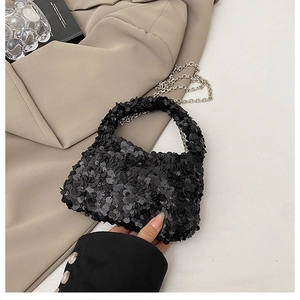 Detail shot of mini black sequin handbag with silver chain on beige blazer background