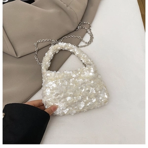 Detailed view of white sequin handbag with silver chain strap on khaki coat background