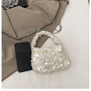 Detail of white sequin cloud bag with silver chain strap beside a smartphone for scale
