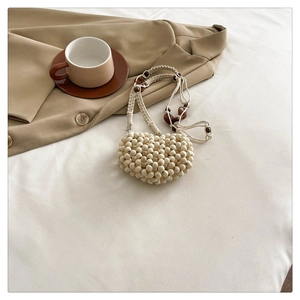 Detail of cream woven heart-shaped beaded bag with amber resin accents on casual bedding