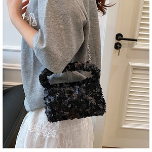 Detail of a sparkling black sequined handbag with a silver metal chain on a model