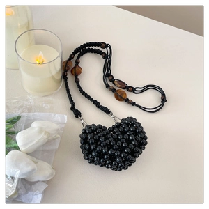 Detail of heart-shaped black beaded crossbody bag with woven rope strap and beads