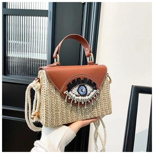 Détail du sac en paille tressée avec rabat en cuir et broderie œil en paillettes
