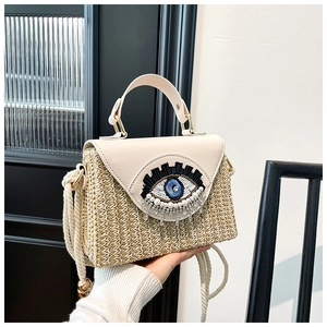 Détail du sac en paille tissée avec rabat en cuir et motif d'oeil orné de perles