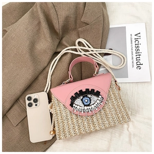 Détail de la broderie œil à paillettes sur un sac en paille avec cuir rose