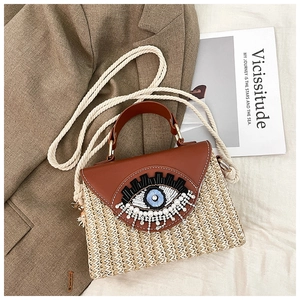 Détail du sac en paille tressée avec broderie Evil Eye, cuir brun et bandoulière corde