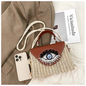 Détail macro du sac en paille avec broderie œil et rabat en cuir marron élégant