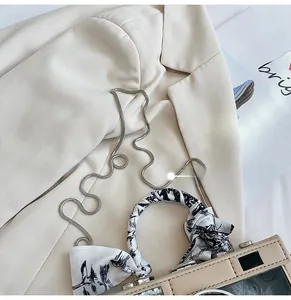 Detail of camera-shaped crossbody bag with snake chain strap and silk scarf handle