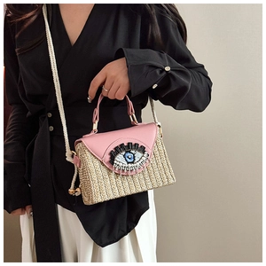 Détail du rabat en cuir rose avec broderie œil et texture paille du sac tressé