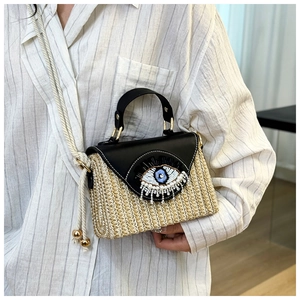 Détail du sac en paille avec motif œil brodé et bandoulière en corde de coton blanc