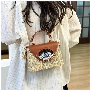 Détail du sac panier tressé avec broderie oeil et pompons en perles porté par un mannequin