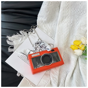 Detail of orange camera-shaped handbag with glossy finish and silk scarf chain strap