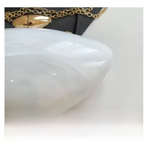 Detail of white marble acrylic clutch featuring a glossy gold clasp and chain strap