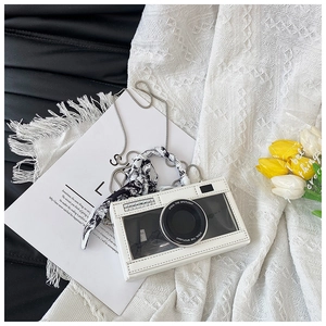 Detail of camera-shaped bag with black lens decor and silk scarf chain strap