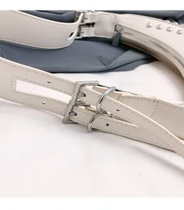 Gros plan sur la boucle argentée et les rivets d'un sac à bandoulière beige en similicuir