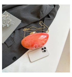 Detail of orange marble acrylic handbag with gold clasp and chain on grey blazer