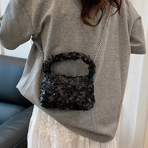 Fashionable black sequin handbag with silver chain strap worn by a model in casual style